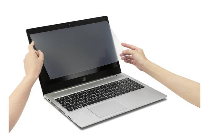 Eine Person befestigt eine Schutzfolie auf dem Bildschirm eines Laptops. Der Laptop ist silber und auf einem Tisch platziert.