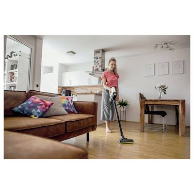Eine Frau saugt den Wohnzimmerboden einer modernen, aufgeräumten Wohnung mit Holzboden und bunten Kissen auf dem Sofa.