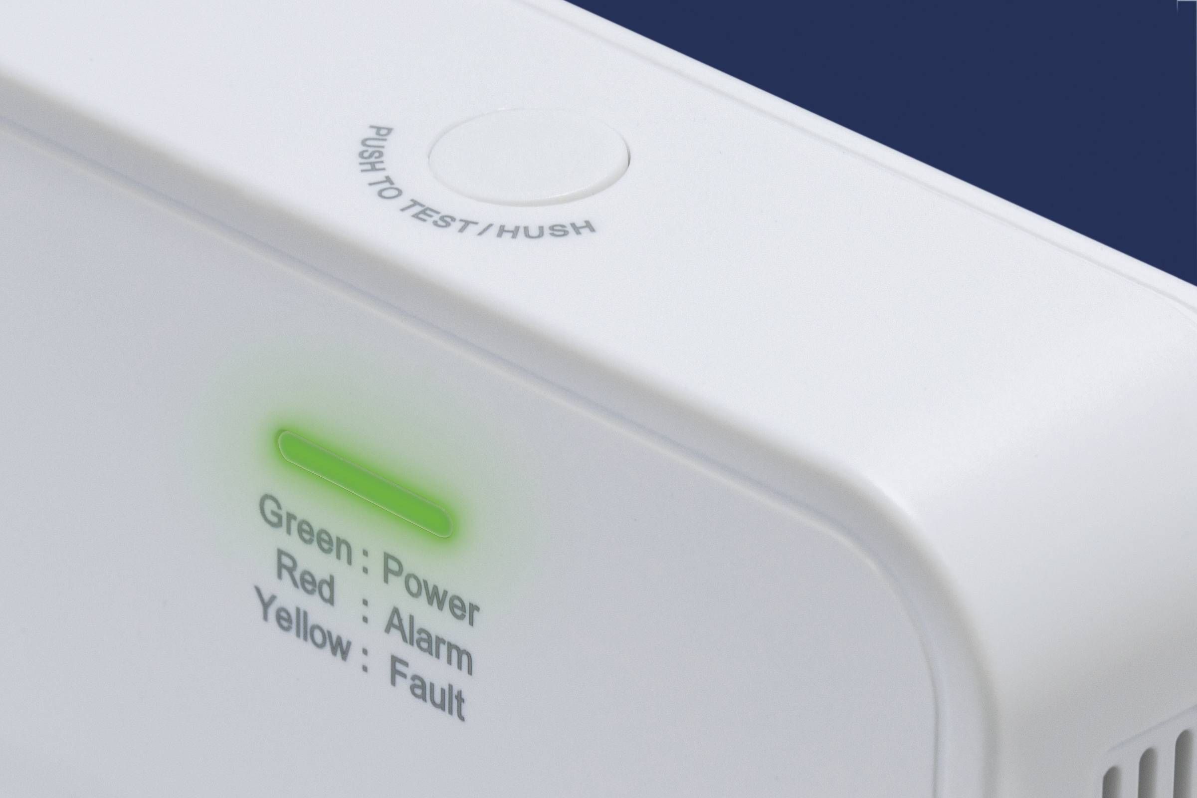 Ein Rauchmelder mit grüner Leuchtanzeige, die den Betriebszustand anzeigt. Oben befindet sich ein Knopf mit 'Push to Test/Hush'.