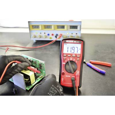 Ein Techniker misst die Spannung auf einer Leiterplatte mit einem Multimeter, das 11,97 Volt anzeigt. Ein Netzteil ist im Hintergrund.