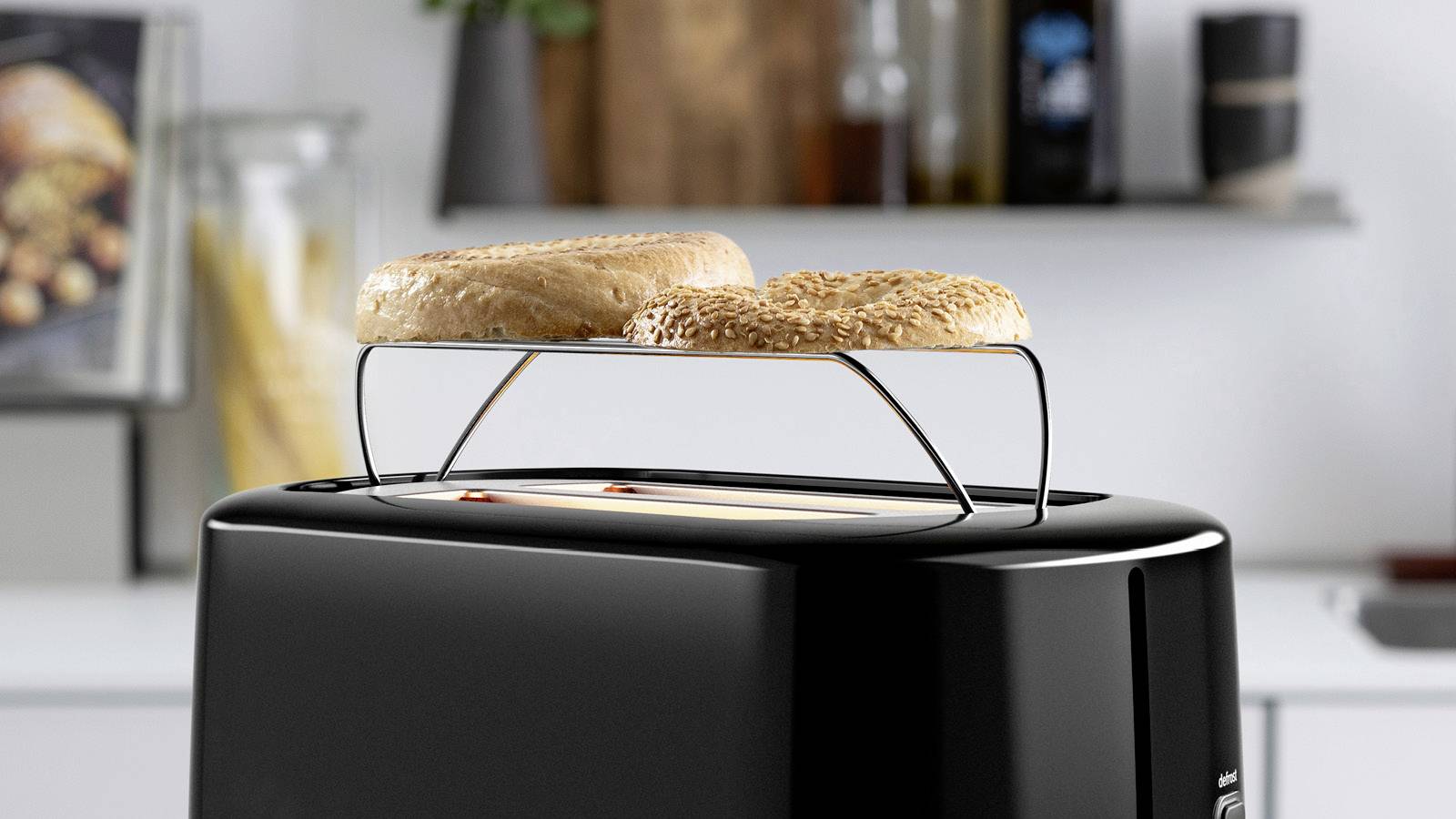 Zwei Bagels auf einem Toaster, in einer modernen Küche mit Pfannen und Gewürzbehältern im Hintergrund.