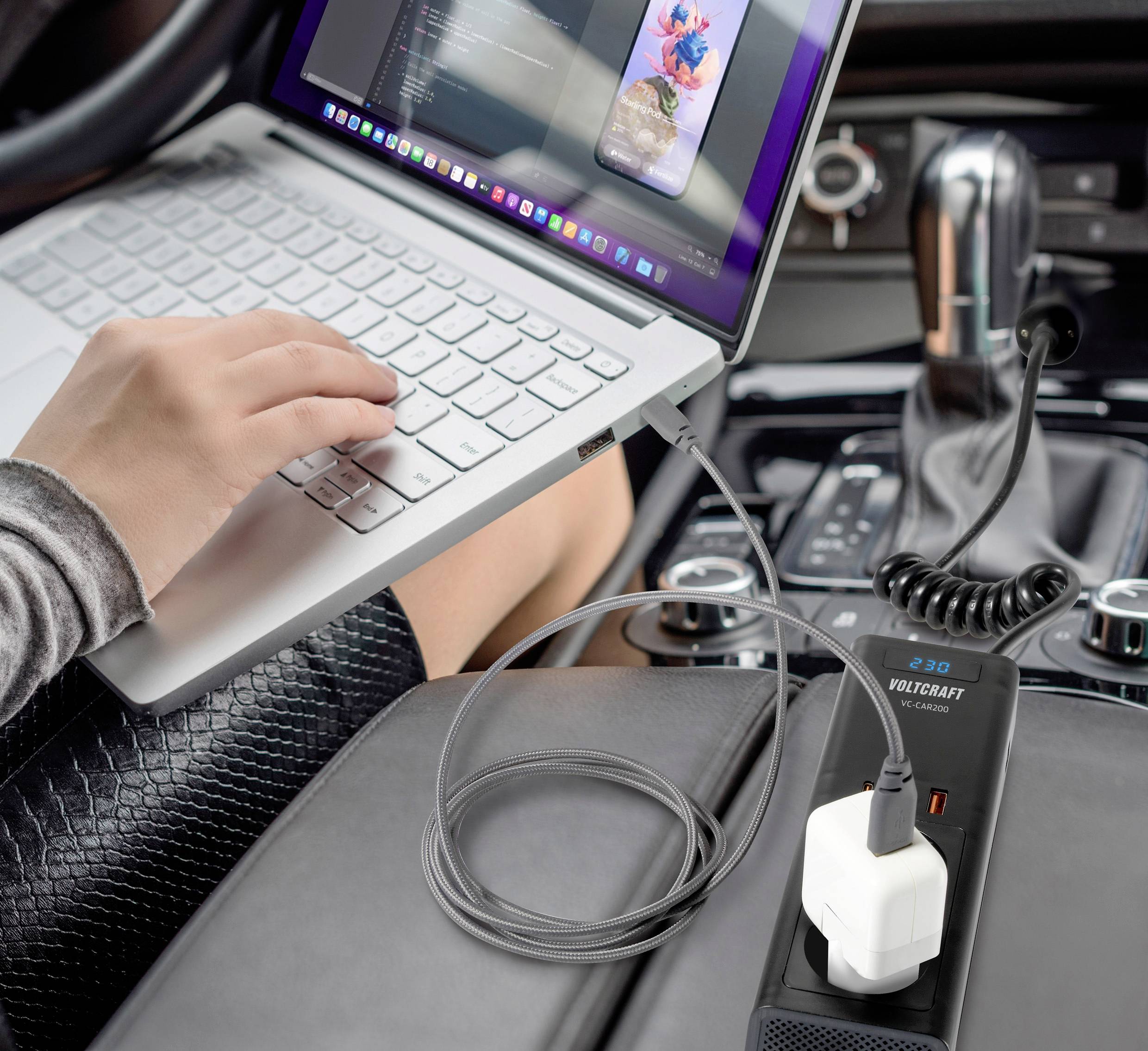 Eine Person arbeitet im Auto auf einem Laptop, der an einen mobilen Spannungswandler angeschlossen ist.