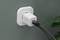 Ein weißer Adapter mit USB-Kabel ist in einer Wandsteckdose eingesteckt. Eine Pflanze ist im Hintergrund sichtbar.