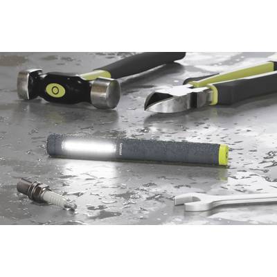 Eine leuchtende Taschenlampe liegt auf einem nassen, metallischen Untergrund, umgeben von verschiedenen Werkzeugen wie Hammer, Zange und Schraubenschlüssel.