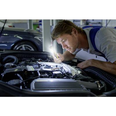 Ein Mechaniker inspiziert mit einer Taschenlampe den Motor eines Autos in einer Werkstatt. Er konzentriert sich auf Details des Motors.