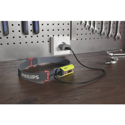Eine Stirnlampe der Marke Philips liegt auf einer Werkbank, angeschlossen an eine Steckdose. Im Hintergrund hängen Werkzeuge an einer Wand.