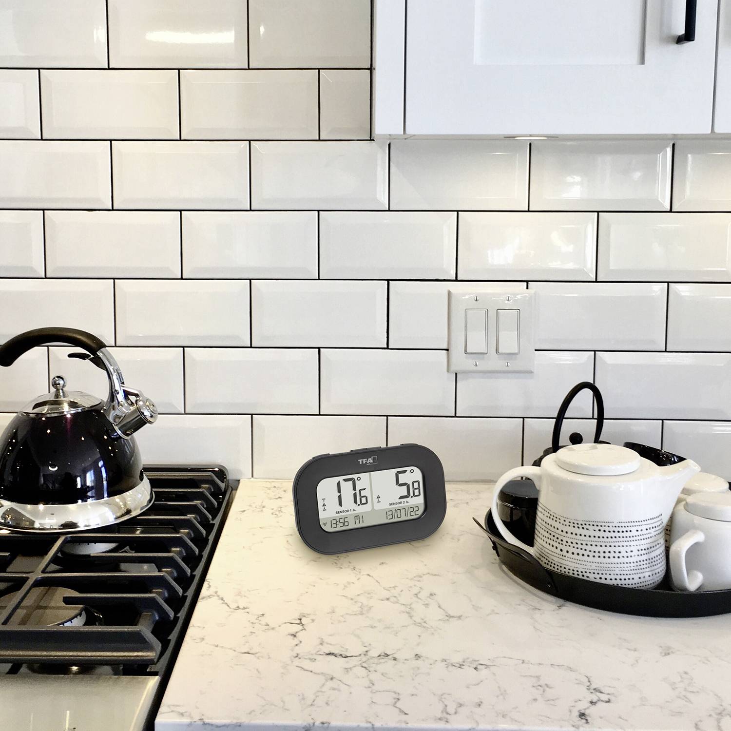 Schwarzer Teekessel auf Herd, digitaler Timer zeigt '17:56 50:12', weiße Teekanne und Tassen auf Tablett, Küche mit weißen Fliesen.