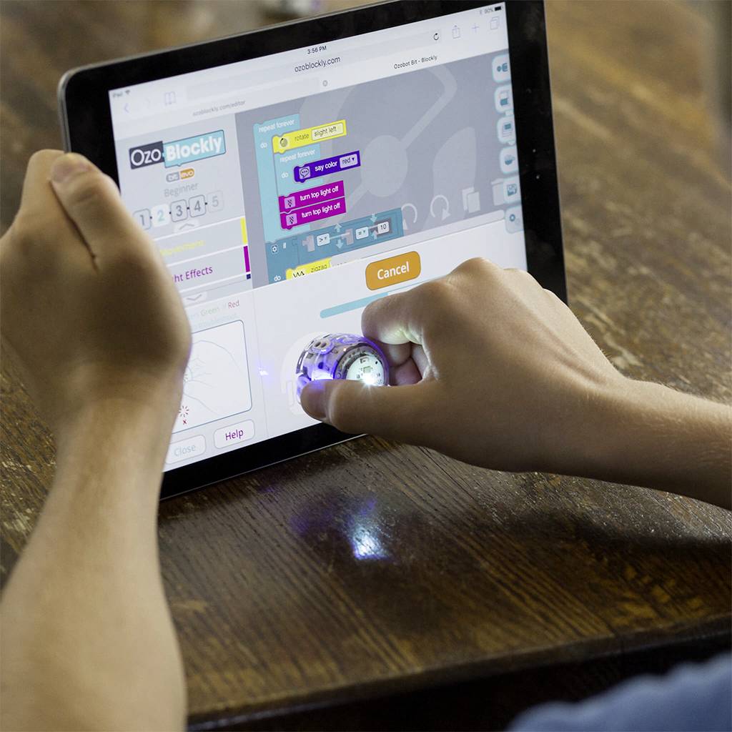 Eine Person programmiert einen kleinen Roboter mit einer Tablet-App. Der Roboter leuchtet und zeigt an, dass er in Betrieb ist.