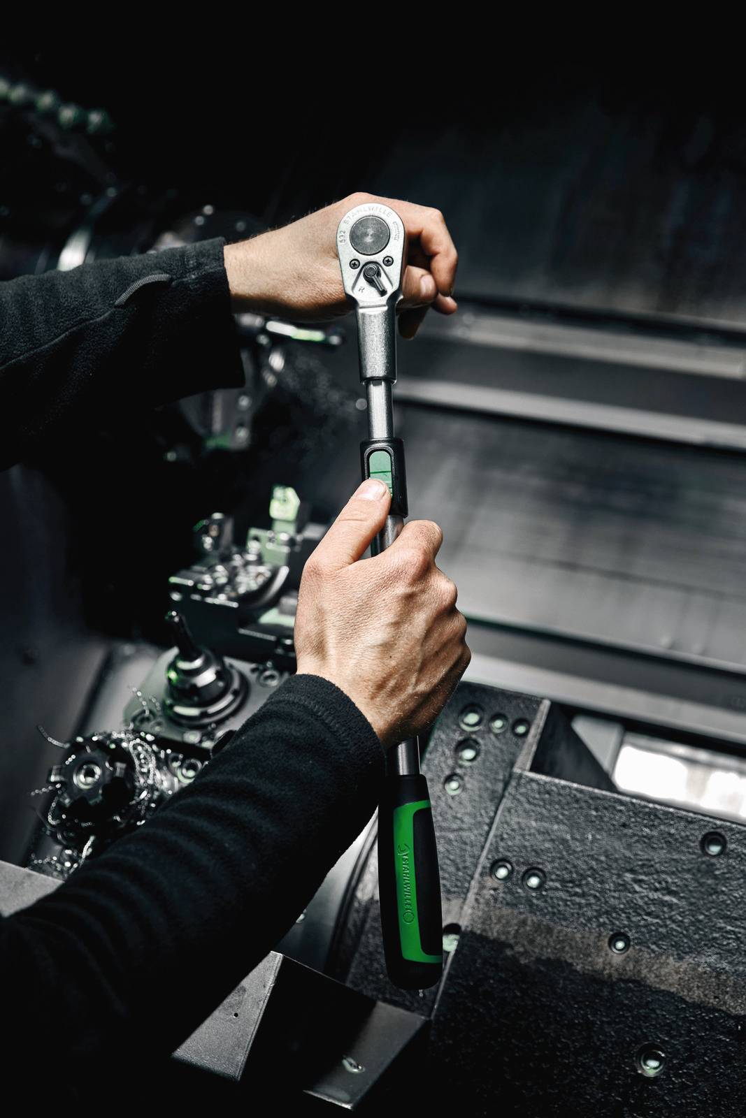 Person bedient mit beiden Händen einen Drehmomentschlüssel in einer industriellen Umgebung, umgeben von Metallgeräten und Maschinen.