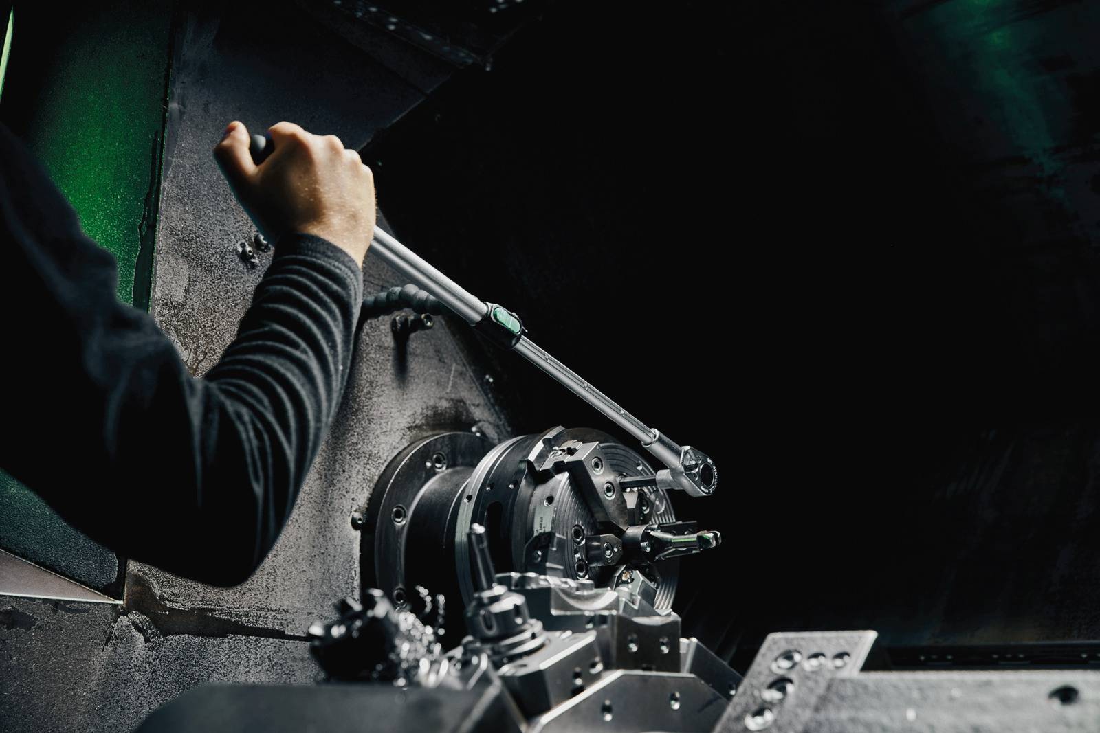 Eine Hand bedient einen großen Hebel an einer Maschine in einem industriellen Umfeld. Die Szene ist dunkel und technisch.