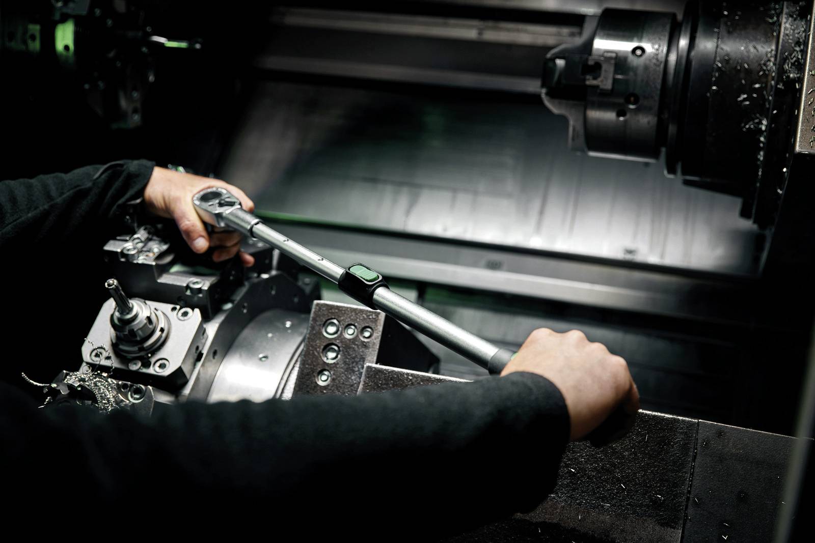 Eine Person arbeitet mit einem Werkzeug an einer Metallbearbeitungsmaschine in einer Werkstatt.