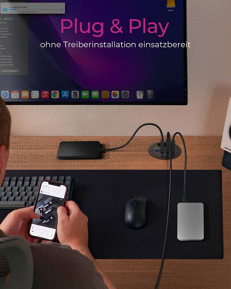'Ein Mann sitzt vor einem Schreibtisch. Er hält ein Smartphone, während er ein Kabel von einem Hub entfernt. Auf dem Monitor steht "Plug & Play ohne Treiberinstallation einsatzbereit".'