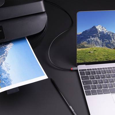 Ein Laptop und Drucker auf einem Tisch. Der Laptop zeigt ein Bergfoto. Der Drucker gibt dasselbe Bild auf Papier aus.
