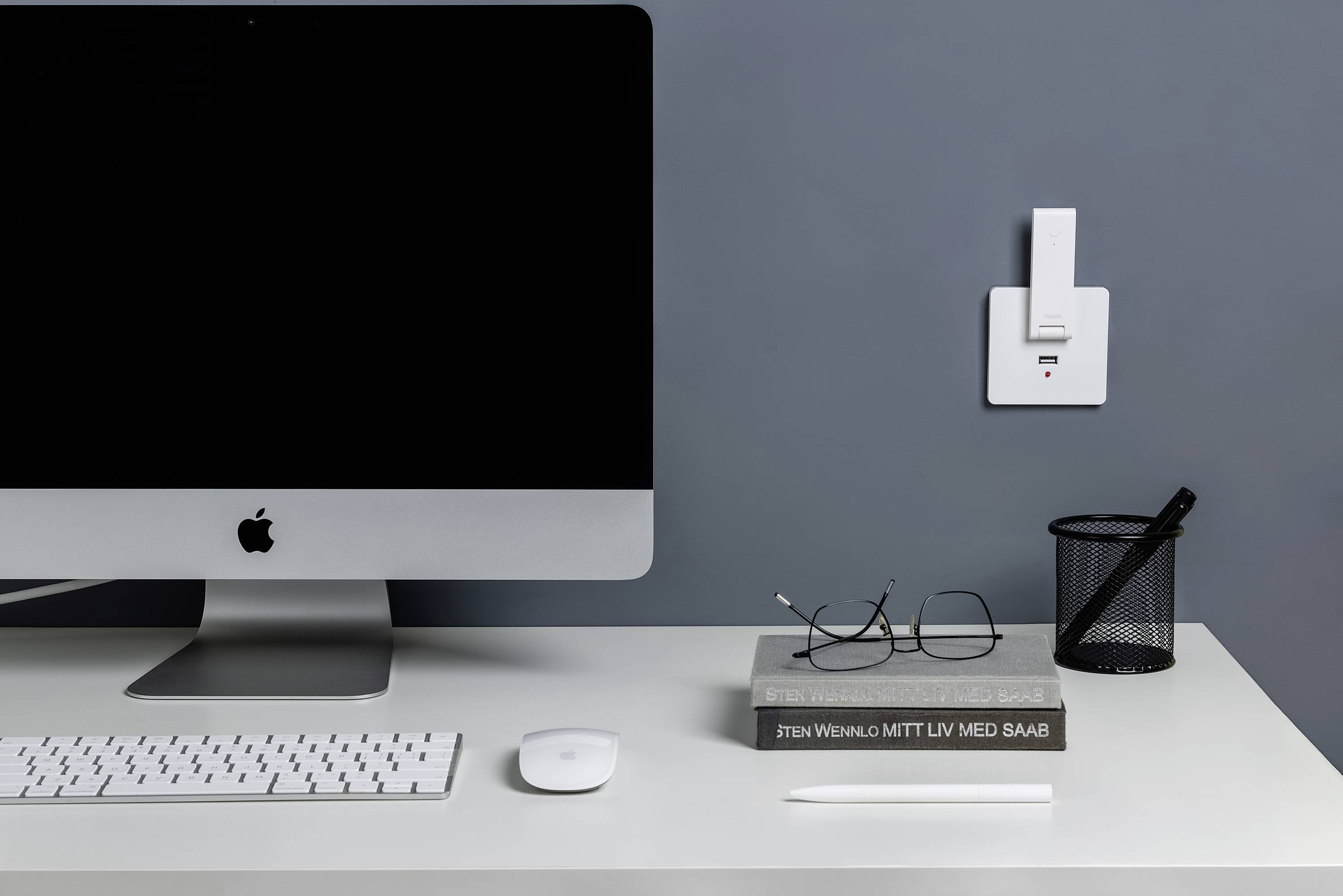 Ein Schreibtisch mit einem Computer, einer Tastatur und einer Maus. Neben dem Computer liegen Bücher, eine Brille und ein Stift.