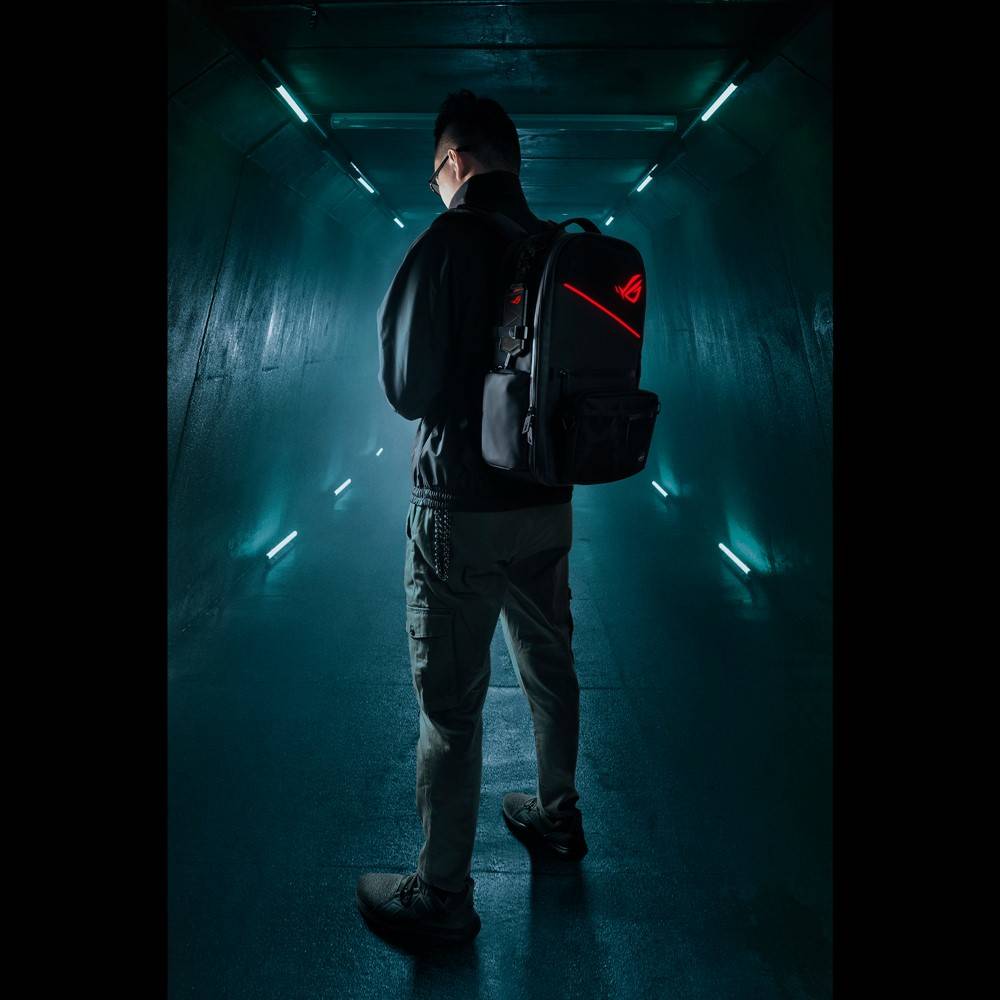 Eine Person mit Rucksack in einem dunklen, futuristischen Gang, beleuchtet von blauen Lichtern, läuft weg von der Kamera.