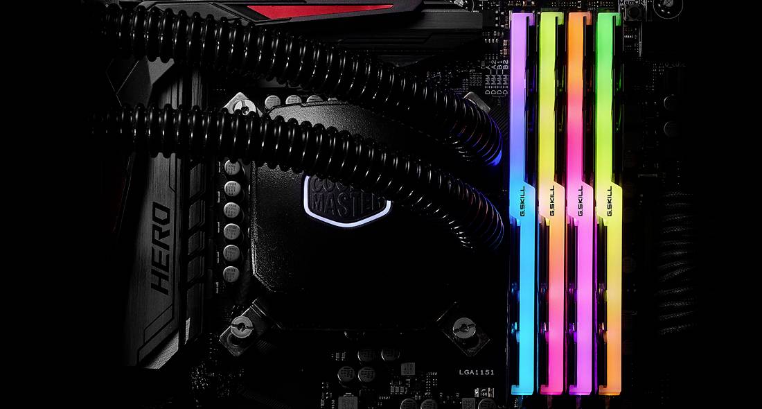 Nahaufnahme eines Computer-Motherboards mit einem Lüfter und vier farbigen RAM-Sticks. Die RAM-Sticks leuchten in verschiedenen Farben.