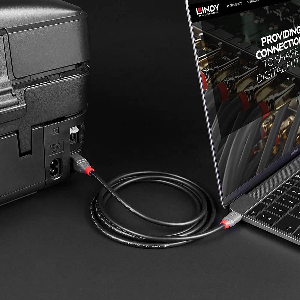 Laptop mit offenem Bildschirm neben einem Drucker, verbunden durch ein USB-Kabel. Anzeigen von Kabel und Anschlussmöglichkeiten.