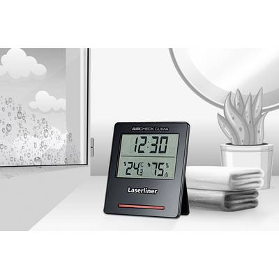 Digitales Hygrometer auf Tisch zeigt '12:30', '24°C', '75%'. Im Hintergrund ein Fenster mit Regentropfen, Pflanzen und Handtücher.