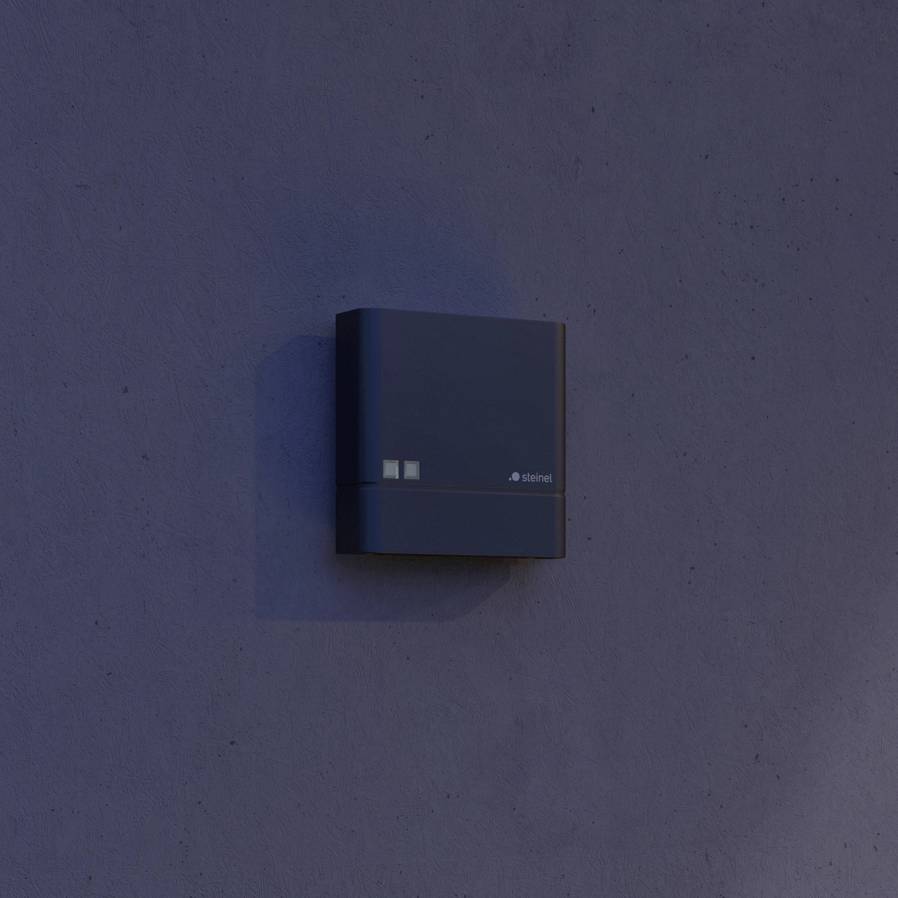 Eine dunkle Box ist an einer blauen Wand montiert. Die Box hat zwei kleine leuchtende Lichter und möglicherweise ein Logo darauf.