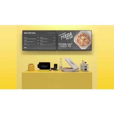 Ein gelber Tisch in einem Imbiss mit zwei Bildschirmen darüber. Links eine Speisekarte, rechts Werbung für Pizza mit Preisangabe.