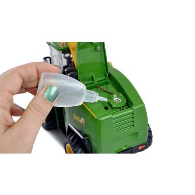Eine Hand füllt mit einer Pipette Flüssigkeit in einen grünen Spielzeugtraktor ein.