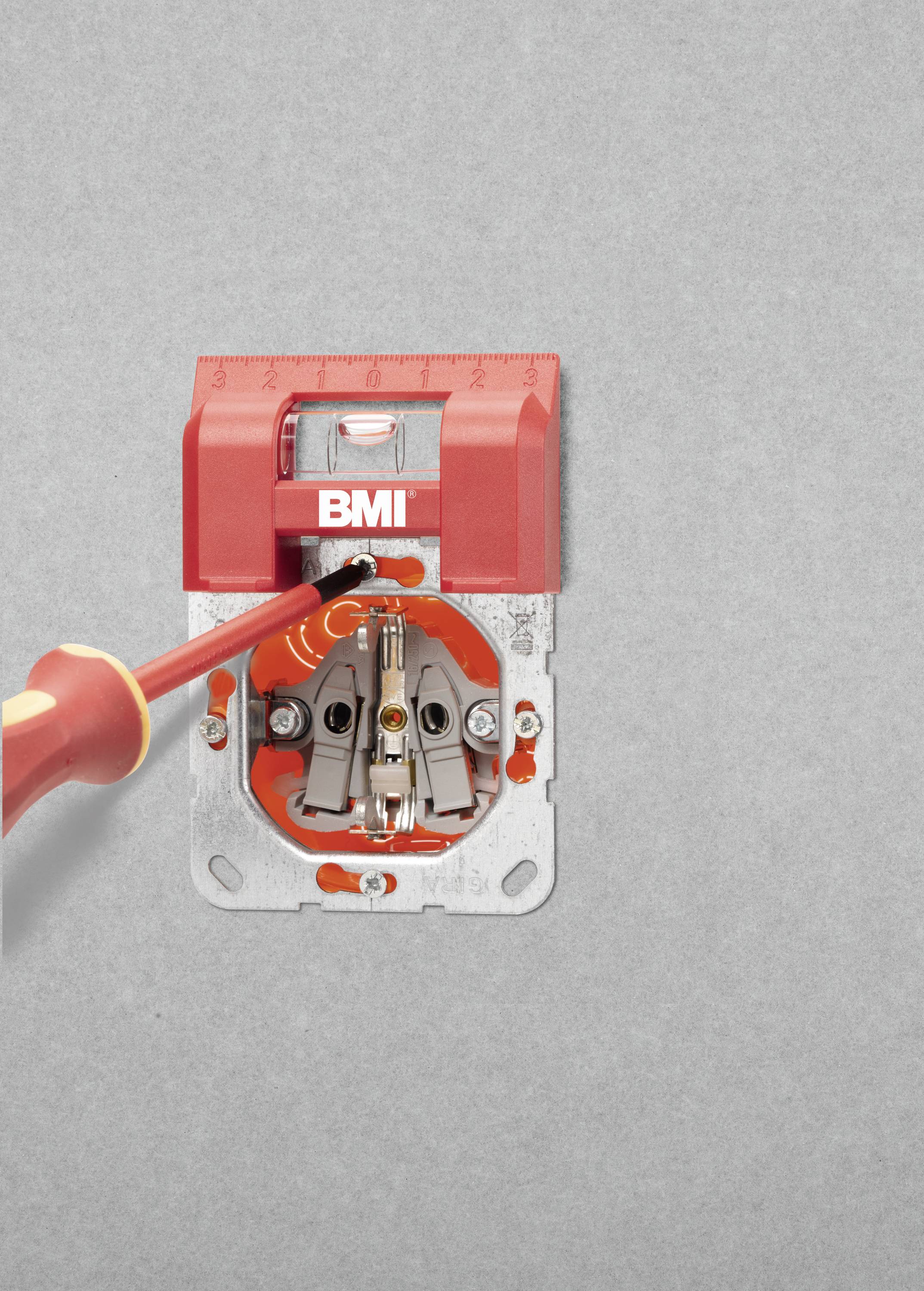 'Ein rotes Messgerät sitzt präzise über einer elektrischen Steckdose mit einem Schraubendreher. Das Gerät misst Neigungen.'