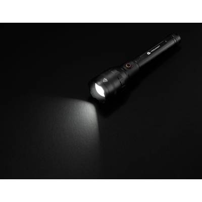 Eine schwarze Taschenlampe liegt auf einem dunklen Hintergrund. Sie ist eingeschaltet und wirft einen Lichtstrahl nach links.
