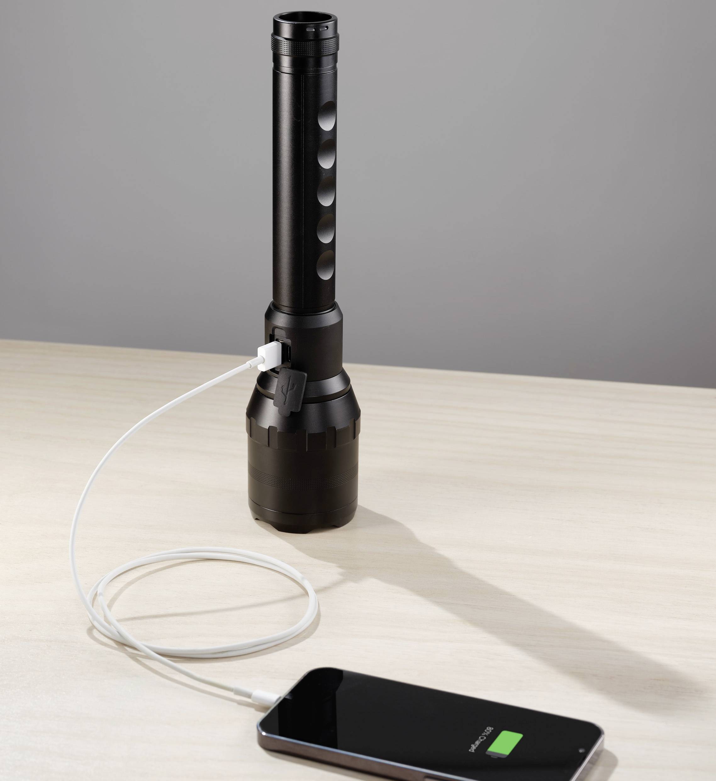 Eine Taschenlampe lädt ein Smartphone über ein USB-Kabel auf, das auf einem Tisch liegt.
