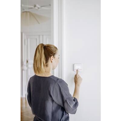 Eine Frau bedient ein digitales Thermostat an einer weißen Wand. Das Display zeigt '20,5 Grad'.