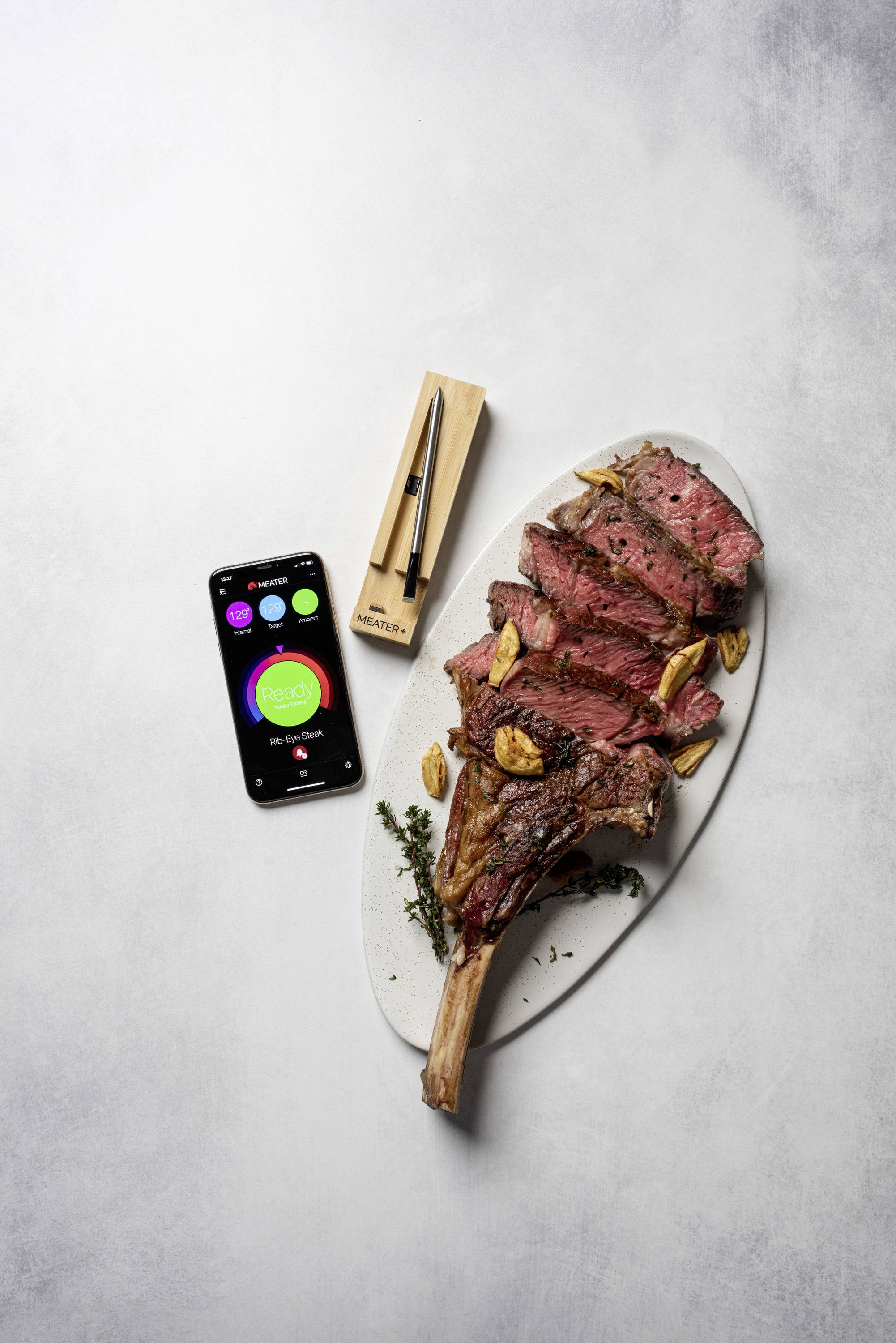 Ein aufgeschnittenes Steak auf einem ovalen Teller, begleitet von einem Smartphone mit einer App-Anzeige und einem Fleischthermometer.