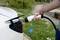 Eine Person hält ein Ladekabel und lädt ein weißes Elektroauto im Freien auf. Im Hintergrund sind Grünflächen sichtbar.