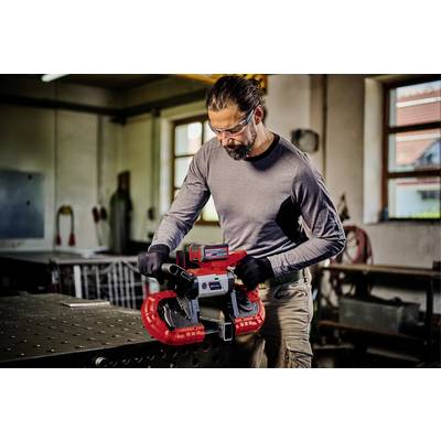 Ein Mann in Schutzbrille und Handschuhen arbeitet an einer industriell aussehenden Bandsäge in einer Werkstatt.