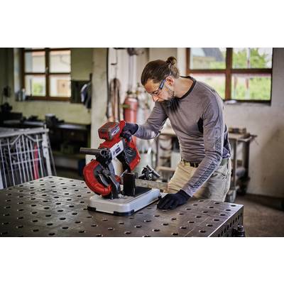 Ein Mann mit Sicherheitsbrille und Handschuhen arbeitet konzentriert an einer Metallbandsäge in einer Werkstatt.
