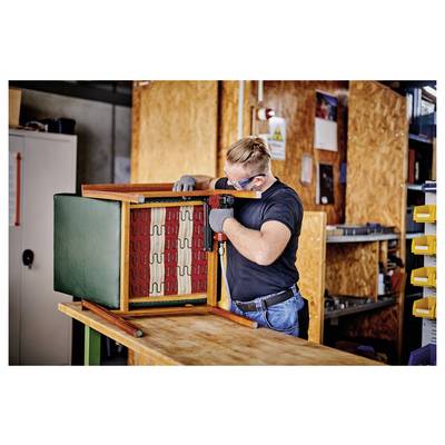 Mann mit Handschuhen und Schutzbrille montiert einen Holzschrank oder Möbelrahmen in einer Werkstatt.