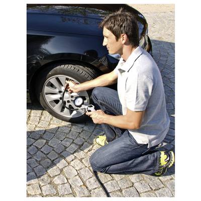 Ein Mann kniet neben einem Auto und verwendet ein Druckmessgerät und einen Schlauch, um einen Reifen auf einer Kopfsteinpflasterstraße aufzupumpen.