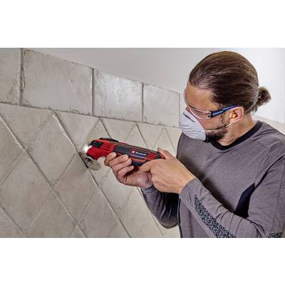 Ein Mann bearbeitet mit einer elektrischen Handwerkzeugfliese an einer Wand. Er trägt Schutzbrille und Maske.
