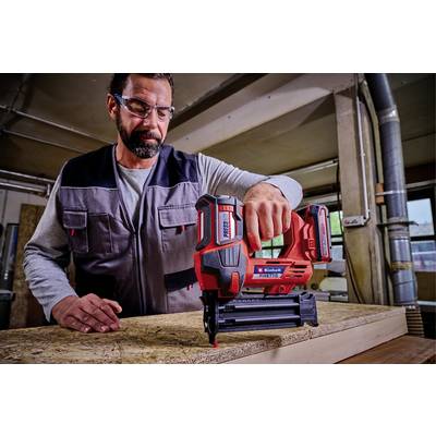 Ein Mann in Schutzbrille und Arbeitskleidung benutzt ein Nagelgerät, um Holzplatten in einer Werkstatt zu befestigen.