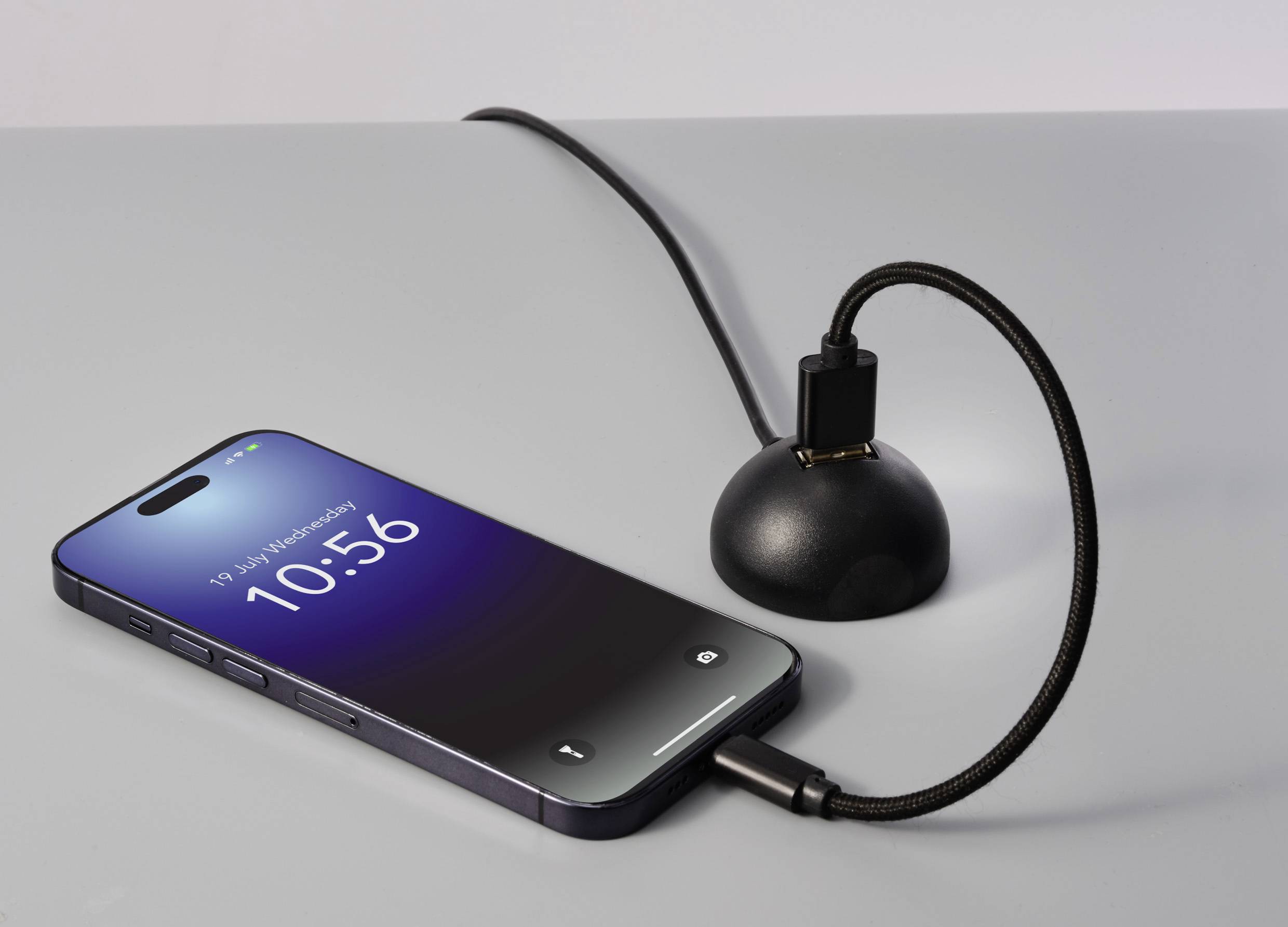 Ein Smartphone liegt auf einem Tisch, verbunden mit einem Ladegerät. Display zeigt Uhrzeit 10:56 und Datum '19 July Wednesday'.