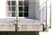 Auf dem Bild ist ein moderner Balkon mit Glasgeländer und Metallpfosten zu sehen. Im Hintergrund reflektieren Fenster das Sonnenlicht.