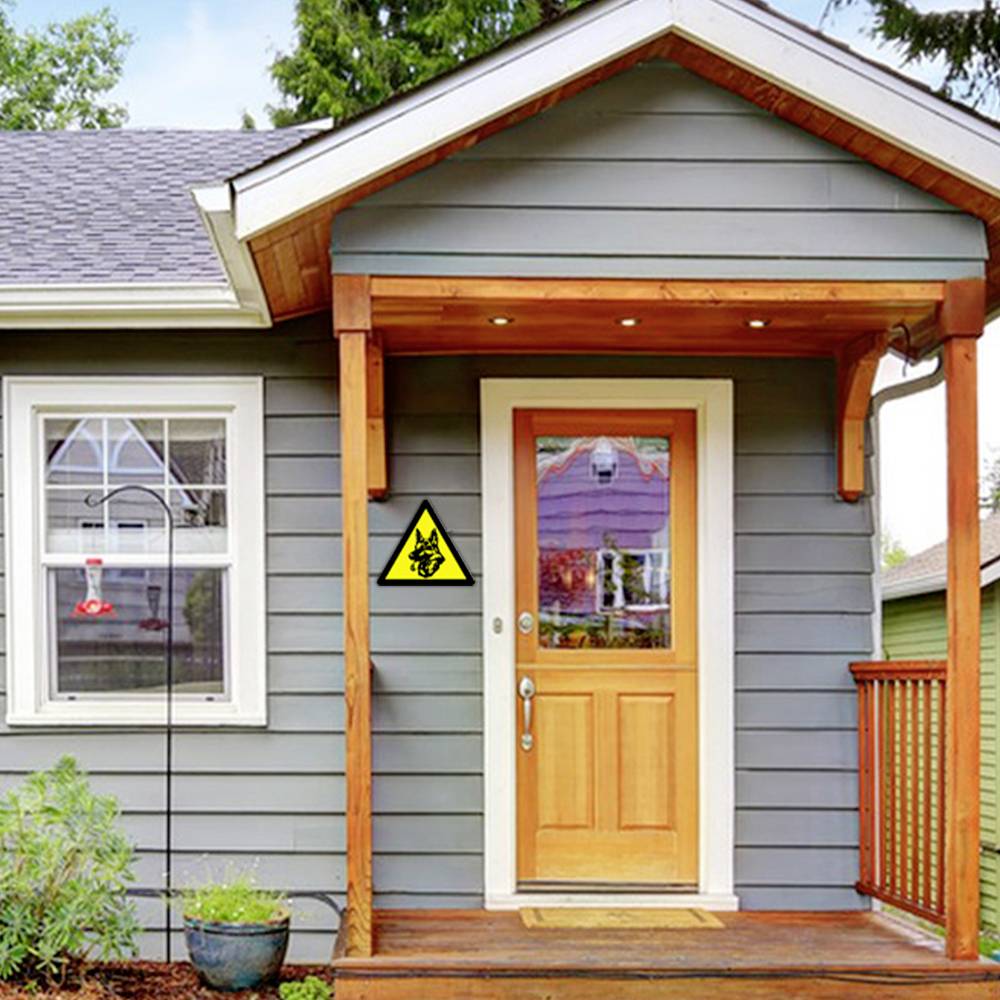 Graues Haus mit Holzveranda, gelbes Schild mit schwarzem Hundesymbol an der Wand neben der Eingangstür.