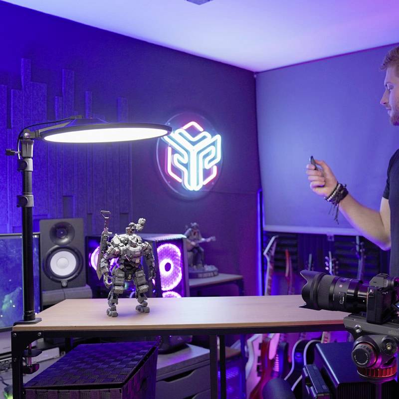 Ein Schreibtisch mit Computer, Lautsprecher und Roboterfigur. Im Hintergrund leuchten Neonlichter, und Gitarren stehen an der Wand.