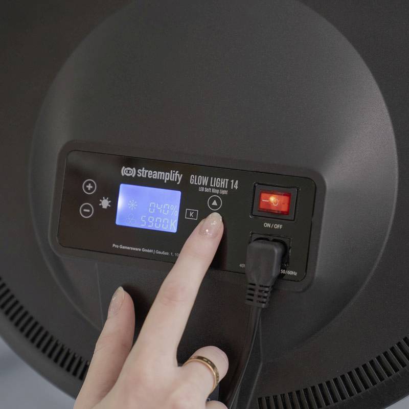 Eine Hand betätigt ein Bedienfeld eines runden LED-Lichts. Das Display zeigt '60% 5900K'. Ein roter Schalter ist auf 'ON'.