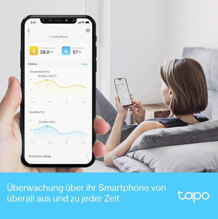 Eine Frau sitzt auf einem Sofa und überwacht mithilfe ihres Smartphones die Temperatur und Luftfeuchtigkeit eines Wohnzimmers.