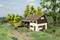 Ein Modellbau-Szenario zeigt ein Bauernhaus mit Strohdach und Holzveranda in einer ländlichen Umgebung. Zwei Figuren stehen vorne, ein Pferd ist in der Nähe.