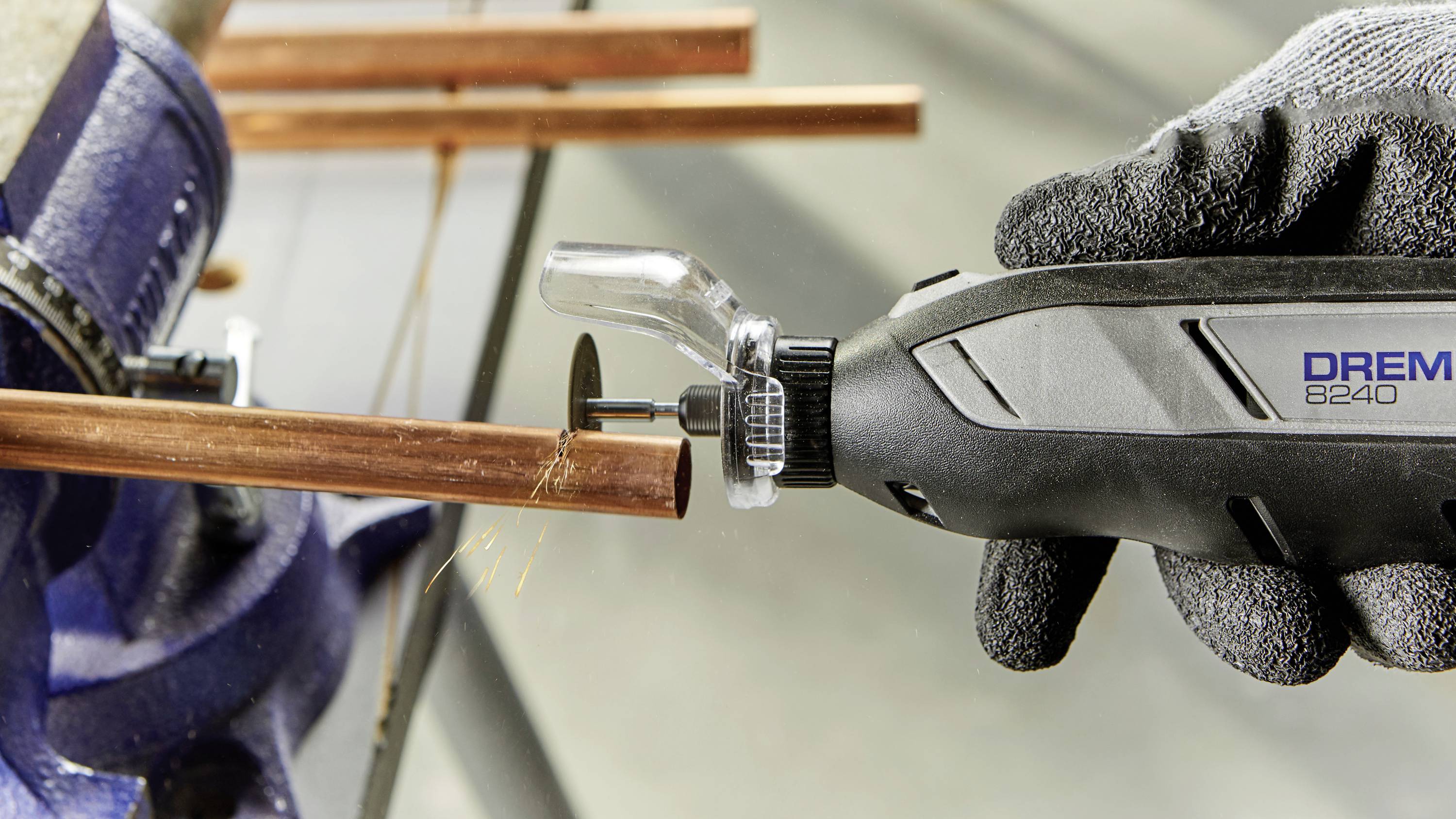 Eine Hand in einem Handschuh hält ein rotierendes Werkzeug, das einen Kupferrohr schneidet. Funken fliegen vom Schnittpunkt.