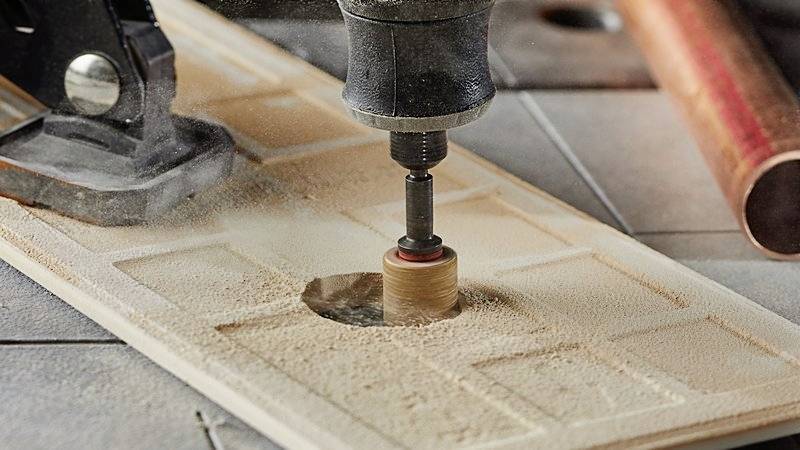 Eine Fräsmaschine bearbeitet präzise eine Holzplatte, dabei entsteht Sägemehl. Die Szene zeigt den Fräsprozess in Nahaufnahme.