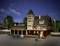 Ein Modellgebäude im Nachbau eines historischen Bahnhofs bei Nacht, beleuchtet von Straßenlaternen. Zwei Figuren beladen eine Plattform mit Gütern.