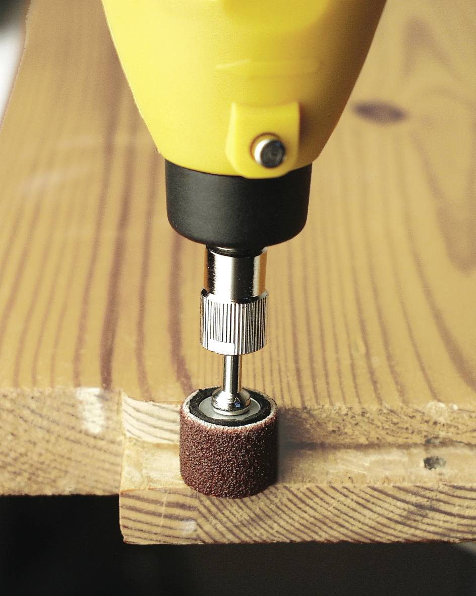 Eine gelbe Bohrmaschine schleift eine Holzkante mit einem Schleifaufsatz. Die Holzkante zeigt deutliche Gebrauchsspuren.