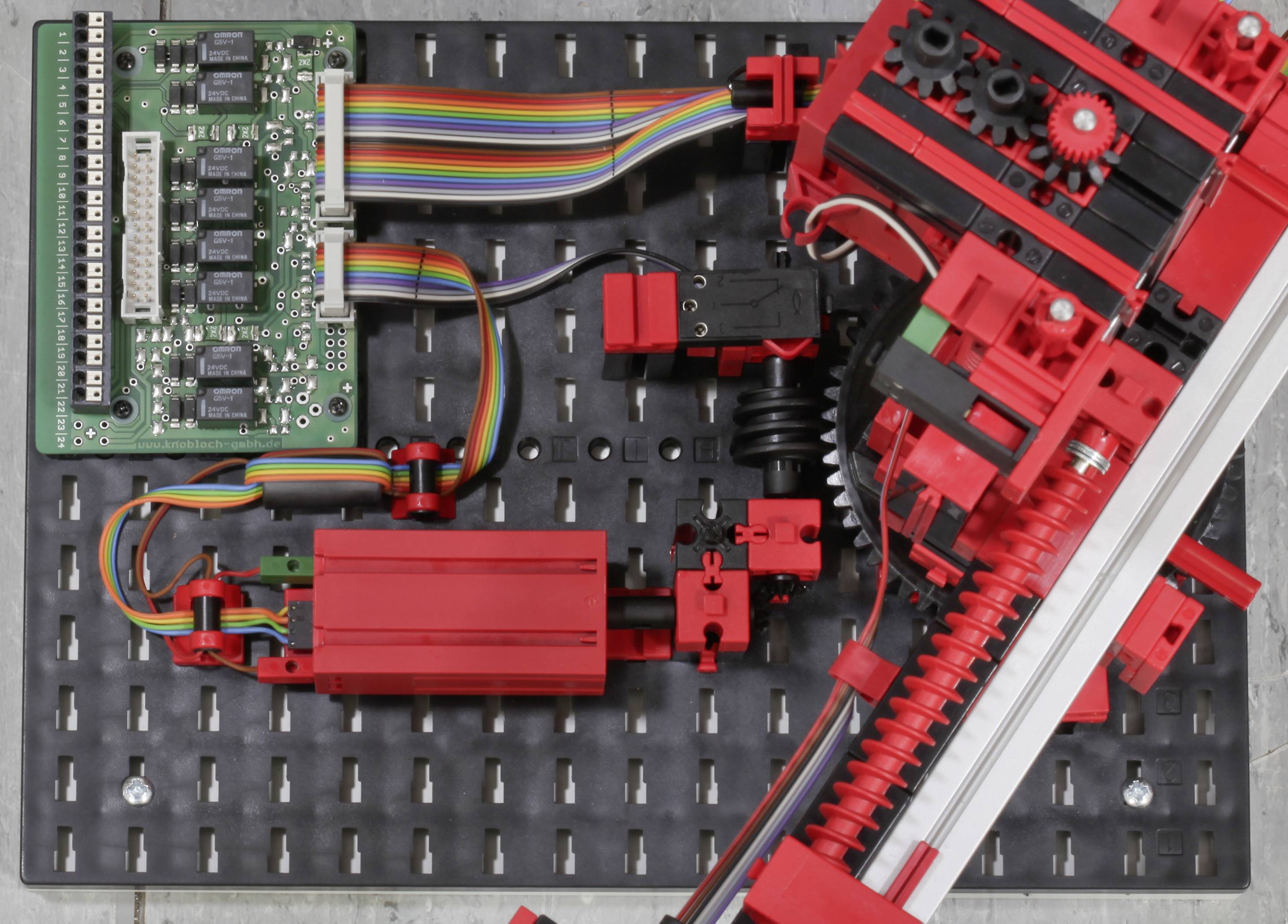 Eine rote Robotik-Konstruktion auf einer Platte mit elektronischen Komponenten und Kabeln.