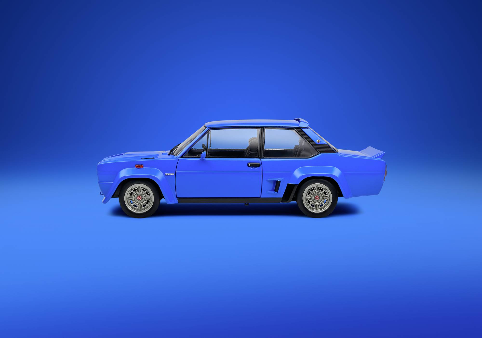 Blaues Auto im Profil vor blauem Hintergrund. Klassisches Design mit zwei Türen und einem auffälligen Heckspoiler. Fahrzeug steht still.